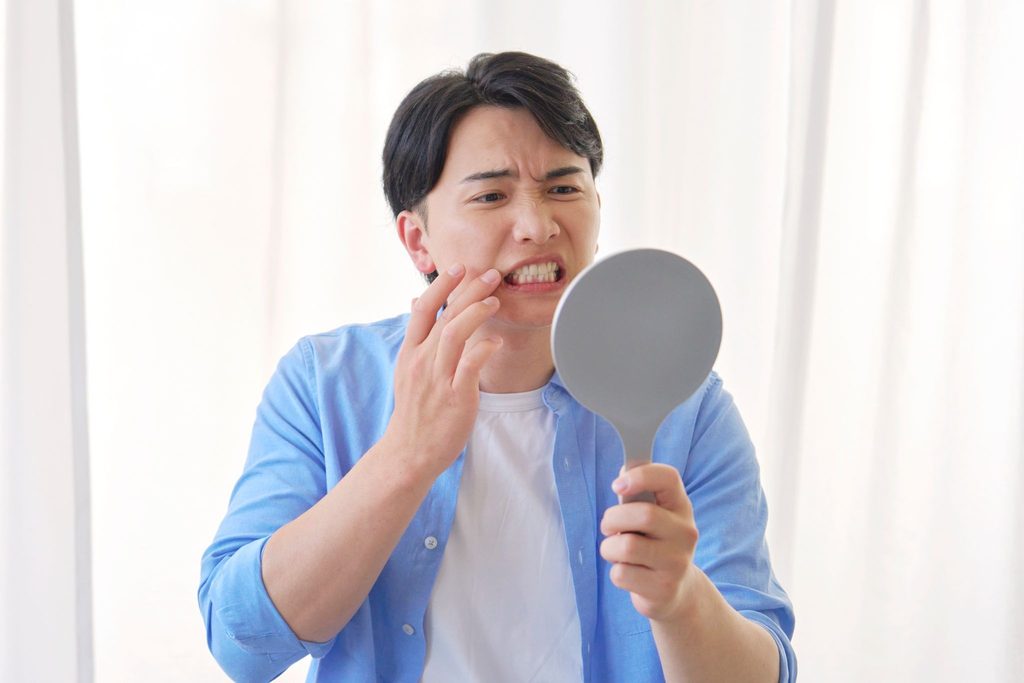 鏡で前歯を気にしている男性