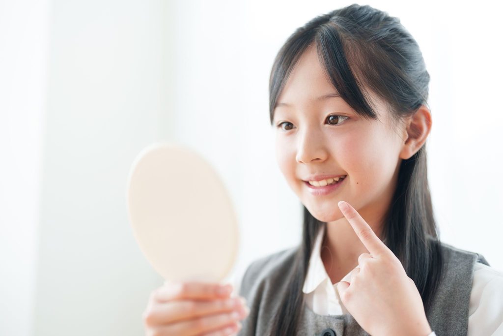 鏡を持って自分の歯並びを見ている子供