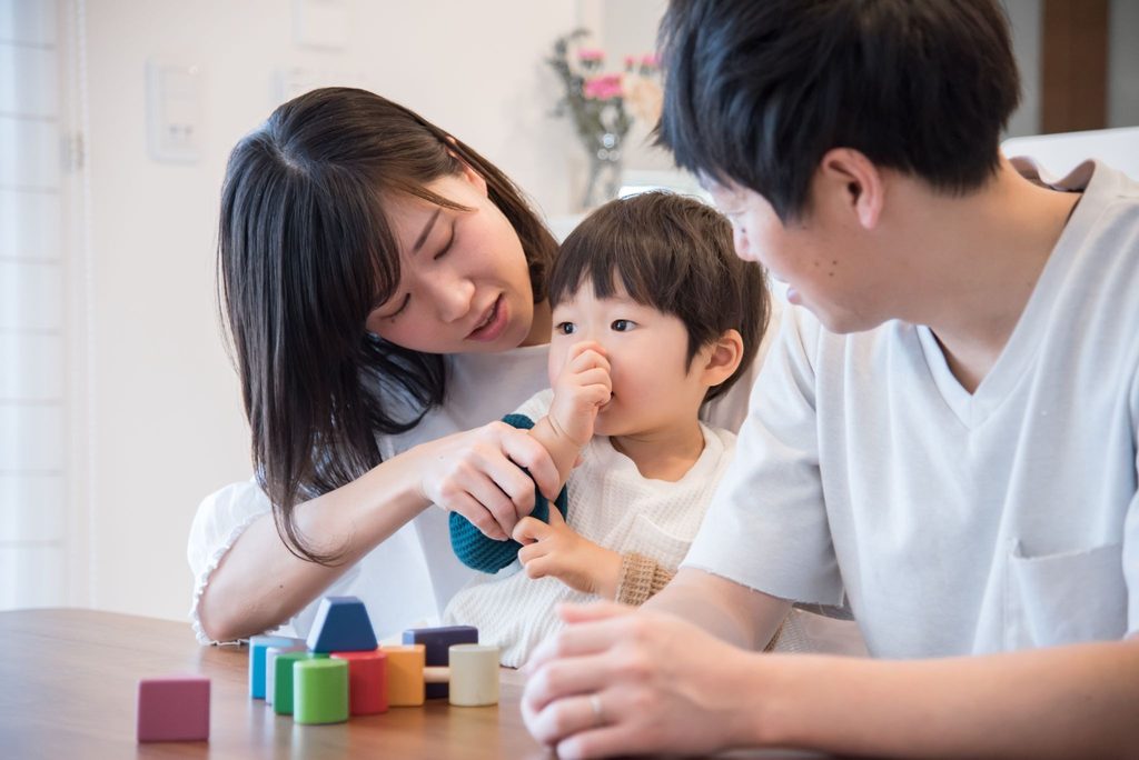 子どもの指しゃぶりをやめさせようとしている母とそれを見ている父