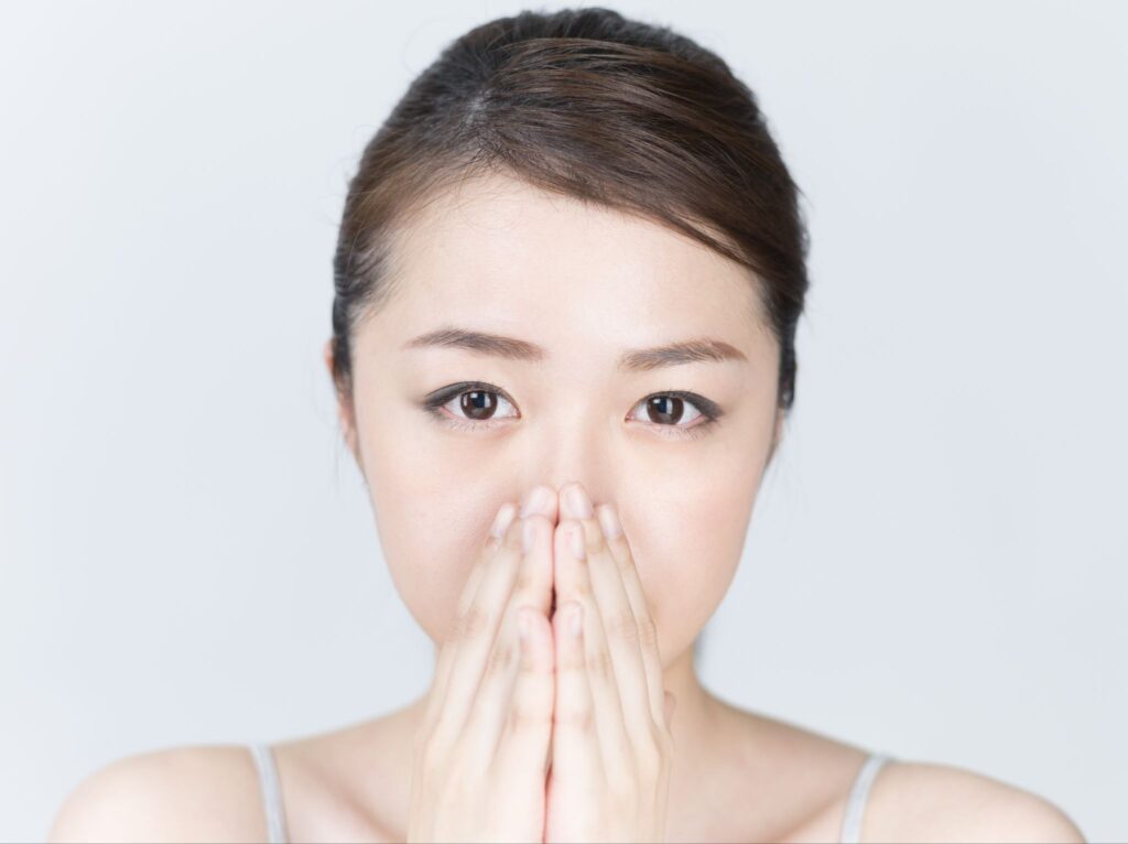 ガミースマイルが気になって口元を隠している女性