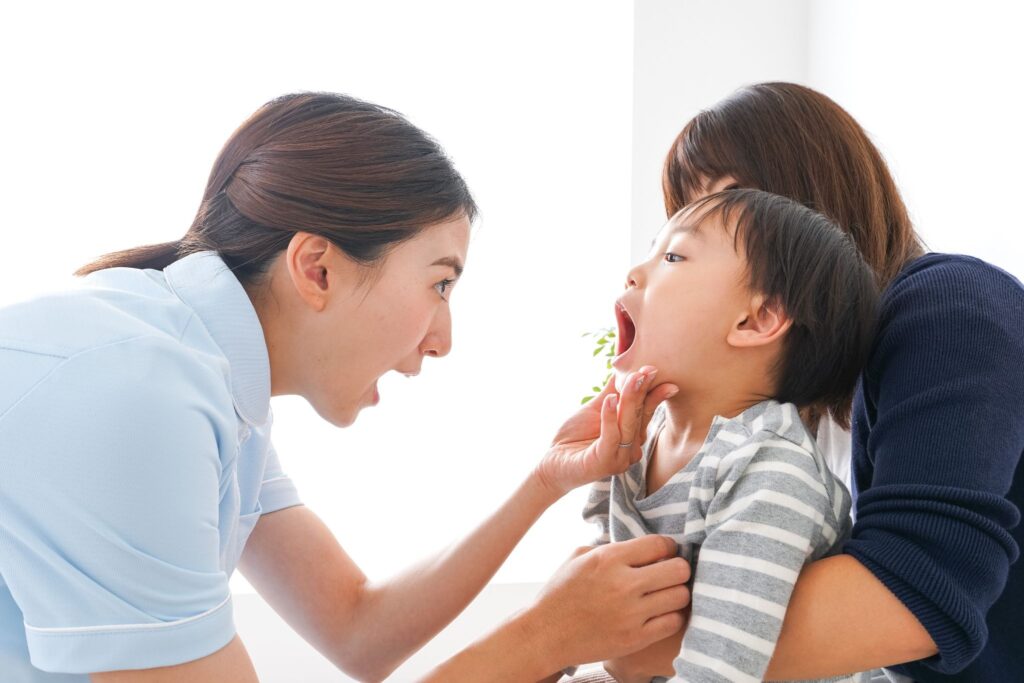 母に抱かれた子どもの口の中をチェックしている医療従事者の女性
