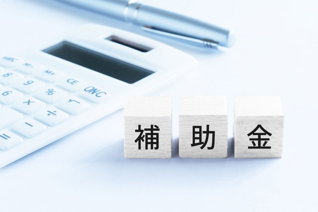 補助金と書かれた木製ブロックと計算機、ペン