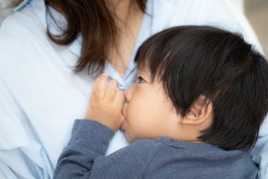 母に抱っこされて指をしゃぶっている子供