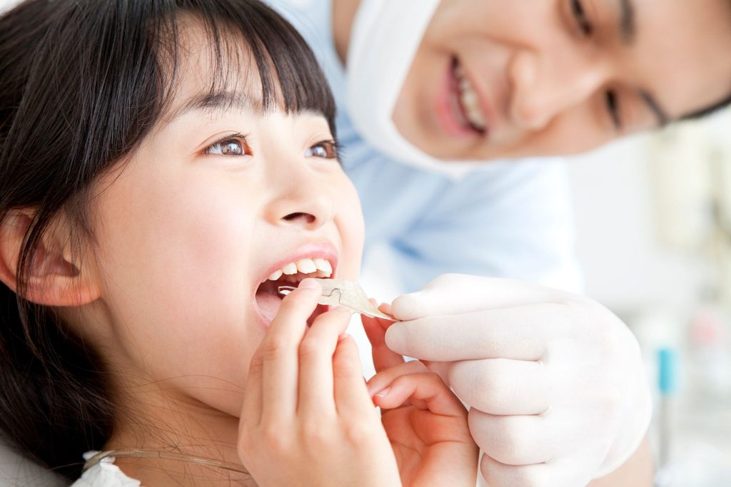 矯正装置を口に入れようとしている子供と矯正歯科医